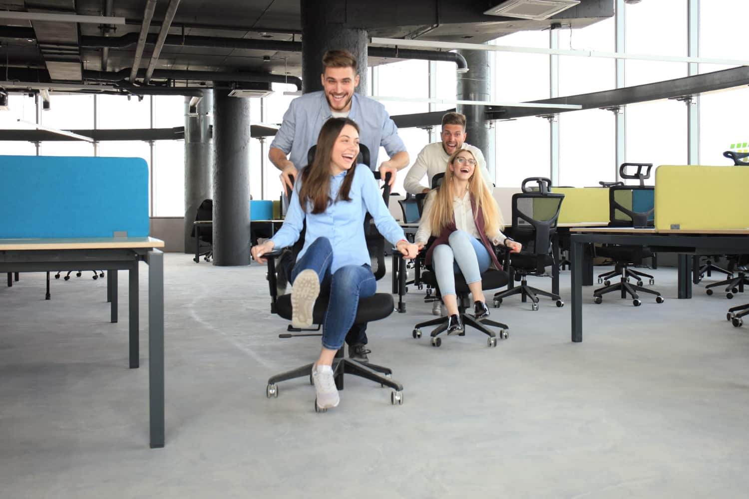 Happy employees pushing each other around in their office chairs.