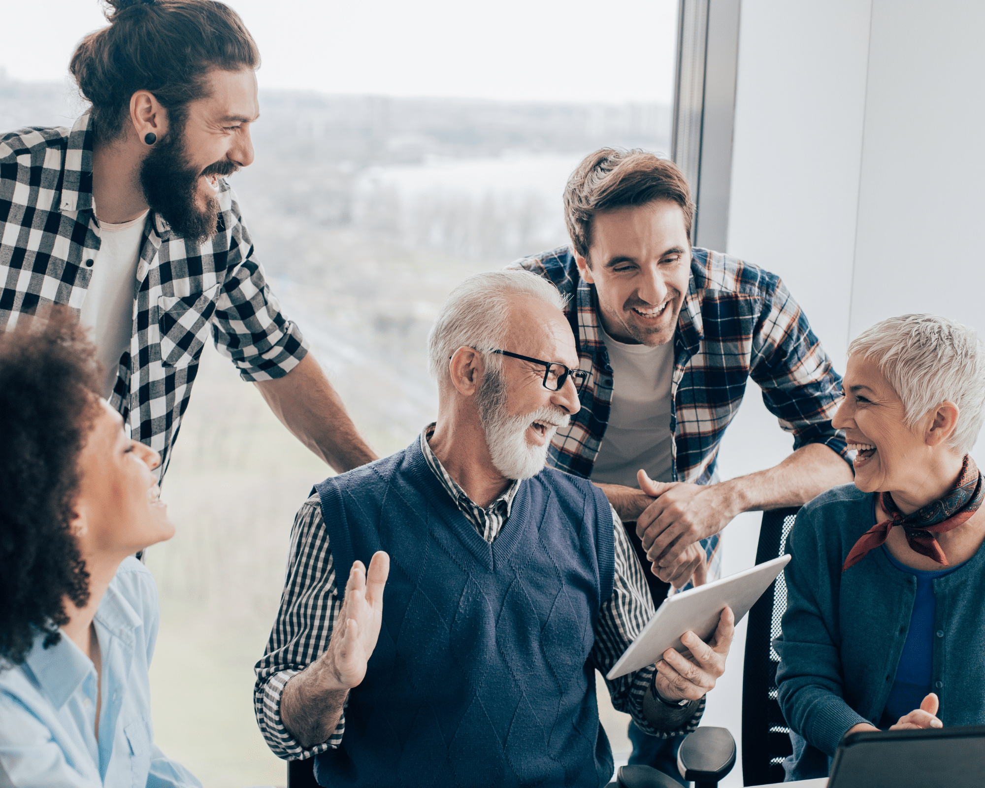 A group of employees from different generations laugh together in the office showing workplace culture can thrive with a focus away from sterotypes